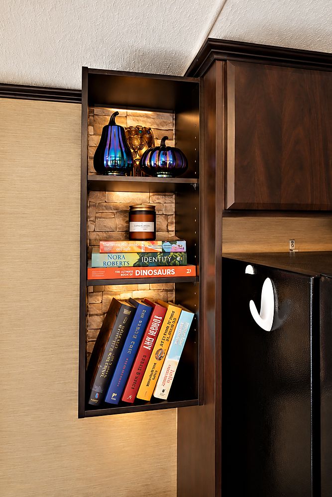 A lit shelf of books and ornaments beside the fridge in Peacedale Cottage